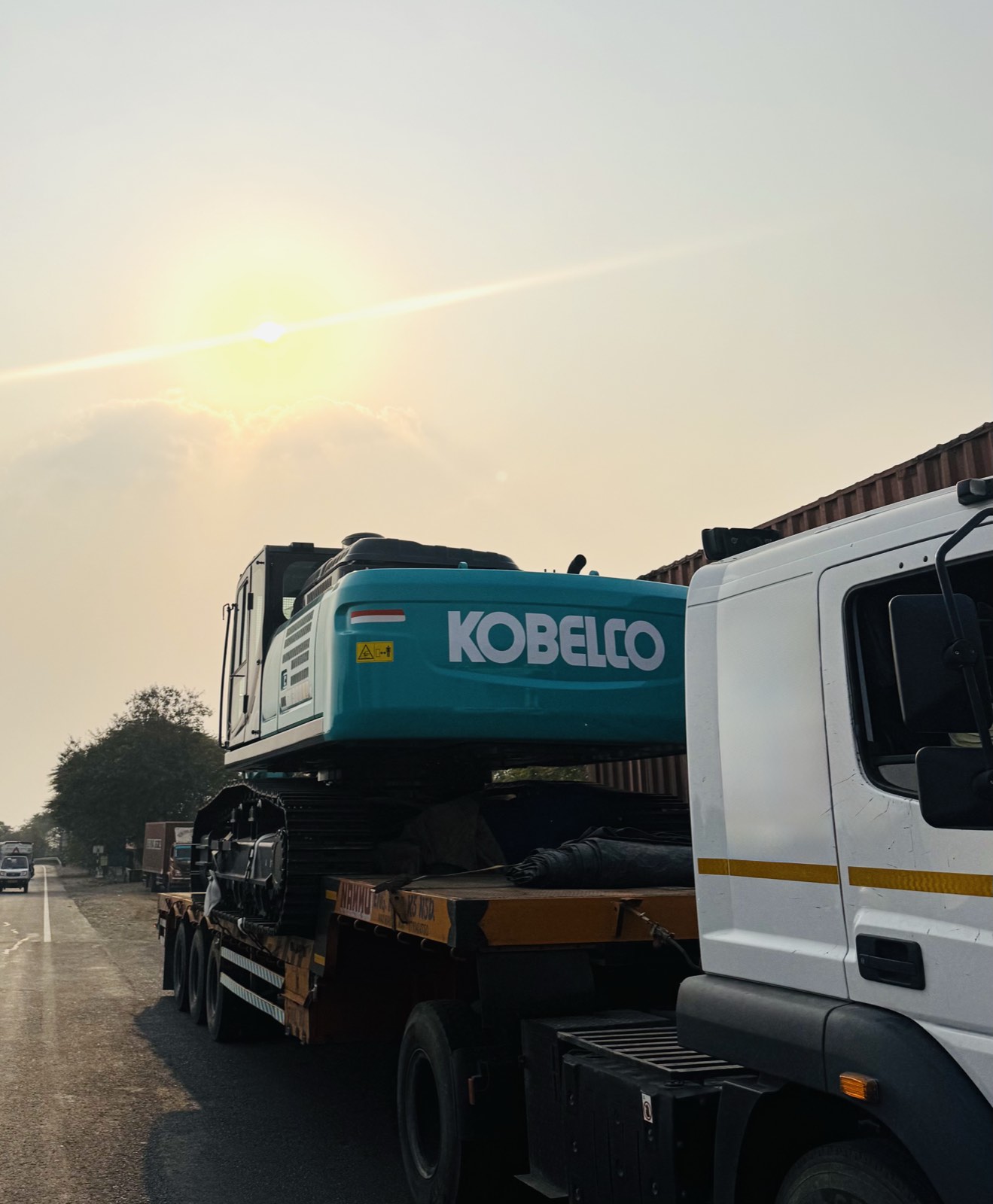Kobelco excavator loaded on a flatbed trailer at sunrise